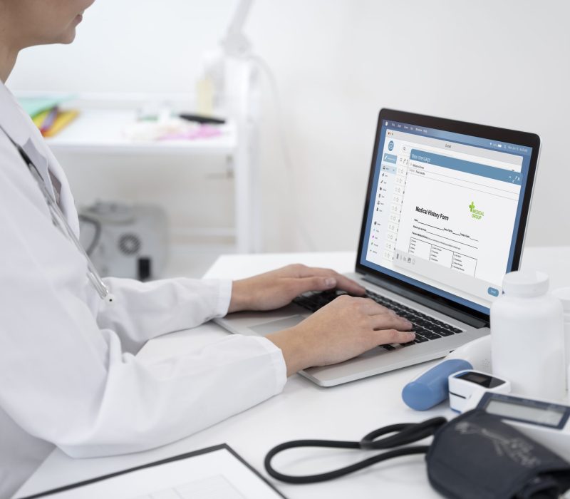 Doctor entering notes on a laptop amid medical devices — Ai scribing streamlines documentation, boosts physician productivity, improves patient satisfaction, and protects revenue..